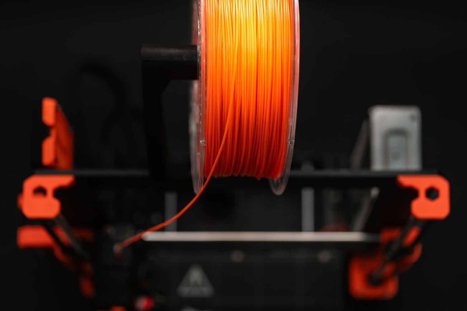 Orange filament spool feeding a desktop 3D printer