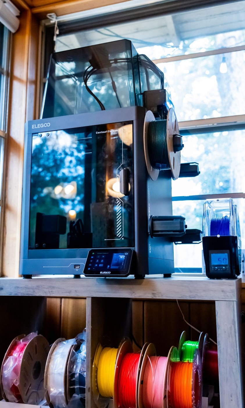 Filament spools stored on a workshop shelf beneath a printer
